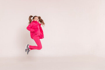 a beautiful girl in a pink jacket jumps and smiles on a white background. happy childhood.