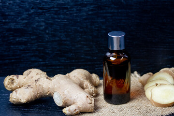 Ginger essential oil in bottle and fresh ginger with sliced on black wooden background. The scientific name is zingiber officinale. Herbs for health care concept.