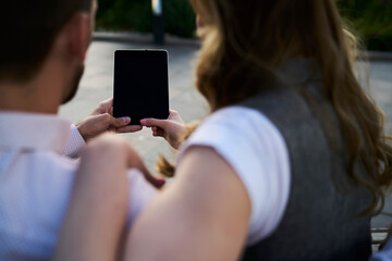 Back view of male and female friends using mockup touch pad technology with copy space area for browsing media content on website, unrecognizable bloggers discussing publication on blank gadget