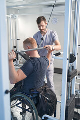 Fototapeta na wymiar Doctor help wheelchair patient on weight machine in physiotherapy room