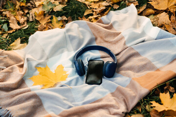 Smartphone mockup, headphones, yellow maple leaf on blanket in autumn park background. Audio...