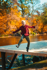A young handsome boy jumps on a panton cheerful in autumn in the park by the lake