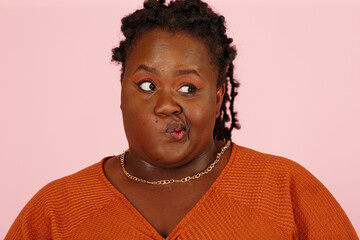 Skeptical young black plus size body positive woman makes a grimace and squints on pink background in studio closeup