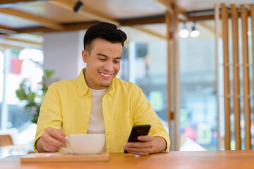 Portrait of handsome young man at coffee shop smiling and using mobile phone