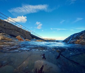 half under the water view of the pier with chalk cliffs in the background, pebbles and sea with blue sky