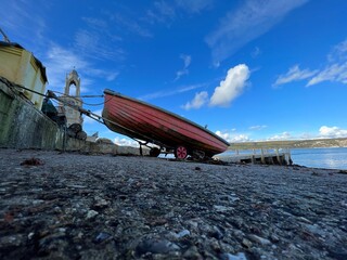 old fishing boat , pink with paint peeling and blue sky on concrete