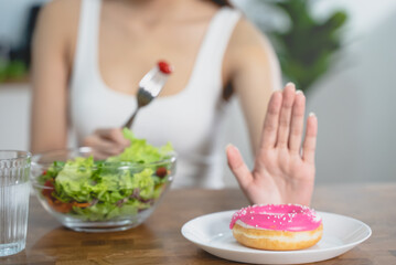 Obraz na płótnie Canvas Woman on dieting for good health concept. Close up female using hand push out her favourite donut and choose salad vegetables for good health.