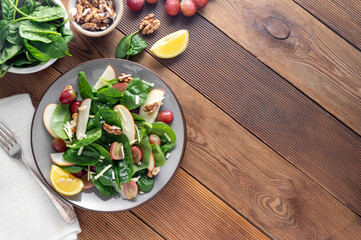Healthy spinach salad made with red apple, wallnuts, grapes. Wooden rustic background, top view