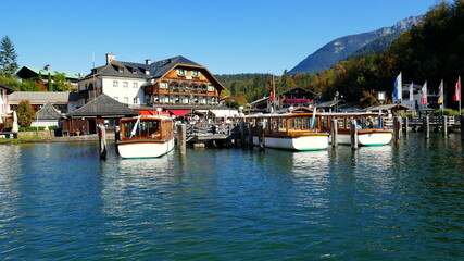Fototapeta na wymiar malerischer Hafen in Schönau am Königssee mit Wald, Hotel und Booten auf blauem Wasser in der Sonne
