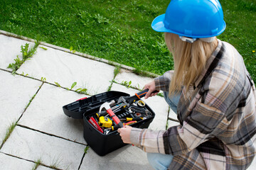 Woman in a helmet with tools. A blond woman is building a house. Female worker. Destroying gender...