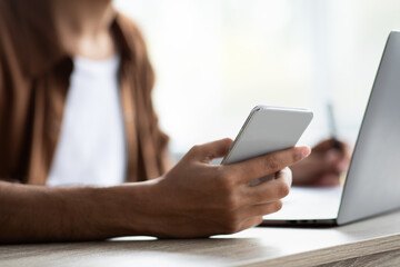 Cropped of man using cellphone while working on laptop