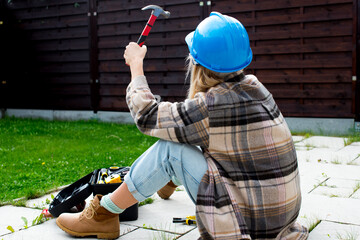 Woman in a helmet with tools. A blond woman is building a house. Female worker. Destroying gender...