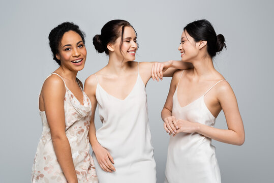 Positive multiethnic women in satin dresses standing isolated on grey