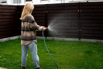 Beautiful blond woman gardening outside. Hydrangea need water. Female gardener with watering can outdoor in backyard. A beautiful woman in her garden, water with a blue watering. Concept of gardening
