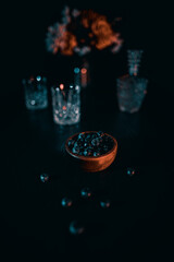 Blueberries on a dark wooden table with flowers and carafe in the background