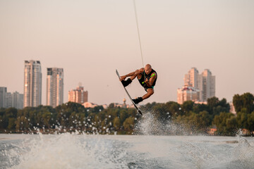 muscular man jumping high with wakeboard on city background.
