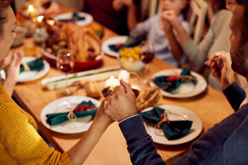 Close-up of extended family holding hands and praying before Thanksgiving meal at dining table,