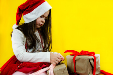 A child in a New Year's costume. Happy child in a New Year's hat on a yellow background. Child on a yellow background. Gifts for the New Year. Child with a gift on a yellow background