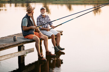 Happy senior man and his son talk while freshwater fishing from pier.