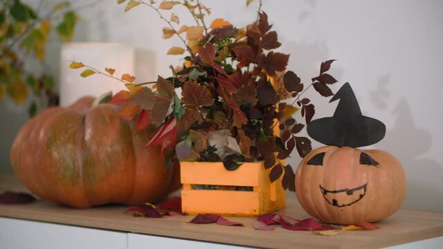 autumn bouquet of leaves in a wooden basket stands on the table next to a painted pumpkin in hat, Halloween decorations