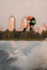 active man holds rope and skilfully jumping high on wakeboard over splashing water.