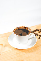 a cup of black coffee on the wooden table with some coffee beans around.  enjoying a morning coffee aesthetically.