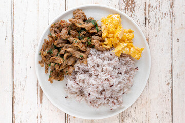 stir fried beef with tree basil leaves, long pepper, Indian long pepper, Javanese long pepper, pepper, garlic, chili beside scrambled eggs and streamed rice on white wood texture background, top view