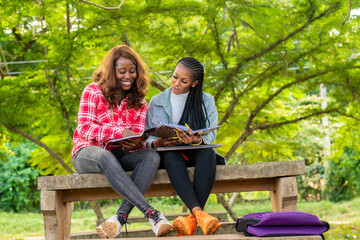 two female african students sitting on a park bench studying