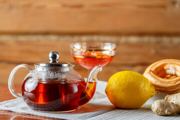 A kettle of strong hot tea on the table on a napkin next to lemon, ginger and jam.