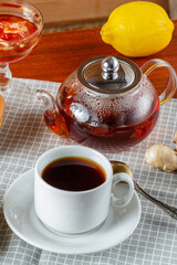 A teapot and a cup of strong aromatic tea on the table next to ginger and lemon ldem and donuts.