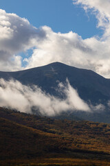 Trees and clouds under the imposing silhouette of the Moncayo mountain in an autumn landscape, Moncayo natural park, Zaragoza, Aragon, Spain