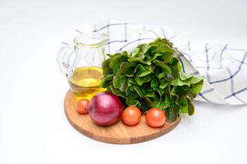 a bunch of green salad, tomatoes, olive oil, ed onion on the wooden board on white background. Ingridients for salad.