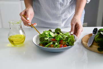 Obraz na płótnie Canvas Woman hands are stirring the vegetable salad on the table.