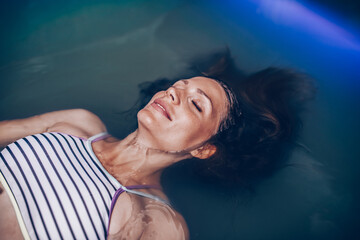 Beautiful pregnant woman floating in tank filled with dense salt water used in meditation, therapy, and alternative medicine.