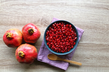 Bowl filled with pomegranate seeds and pomegranate fruit on a table. Flat lay.