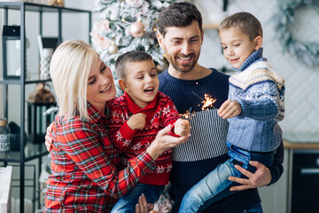 Fototapeta premium . a young family with two children in a cozy room is getting ready for the new year, sparklers are lit.