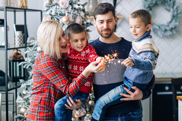 beautiful young parents hold two sons in their arms to light sparklers.