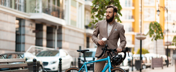 Modern businessman with a bicycle drinks takeaway coffee on the street. Active lifestyle, ecological transport.