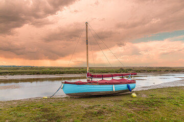A sailing dinghy beside the River Glaven on the salt marshes at Blakeney National Nature Reserve at...