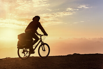 Mountain bicycle rider with backpack travels over sunrise background