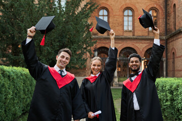 Multinational graduates male and female celebrating graduation in university campus, removing their...