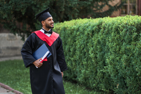 Happy Indian Graduate Walking In University Campus In Robe And Diploma