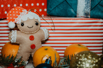 Soft Christmas toy. Gingerbread man's toy on the background of a Christmas gift box with tangerines and Christmas tree decorations