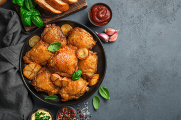 Fried chicken thighs with sauces and spices on a dark background.