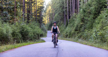 Fototapeta premium Adventurous White Caucasian Woman on a bicycle riding on a path in Green Canadian Rain Forest. Seymour Valley Trailway in North Vancouver, British Columbia, Canada.