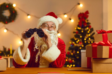Fototapeta na wymiar Father Christmas holding binoculars watching who's been naughty or nice, good or bad this year. Surprised Santa Claus looking out for New Year deals and sales, discounts, amazing gifts and presents