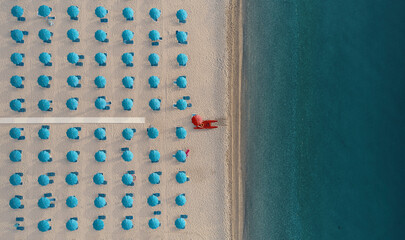 Aerial view of a well sorted lido with blue parasols and sunbeds at sunrise along the coastline in Calabria, Italy.