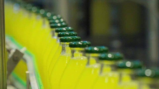 Line of glass bottles on a conveyor belt filled with yellow liquid lemonade