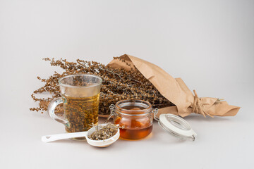 Glass of herb tea, tea strainer, honey and Wormwood twigs wrapped in brown paper.