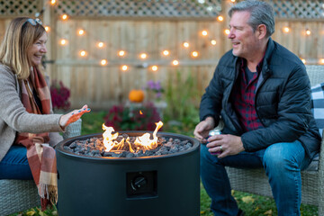 Middle age couple sitting by a backyard fire pit in autumn - 466778763